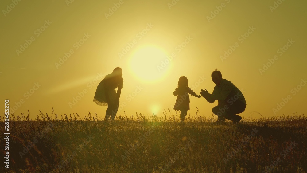 mother and Dad play with their daughter in sun. happy baby goes from dad to mom. young family in the field with a child 1 year. family happiness concept. beautiful sunshine, sunset.