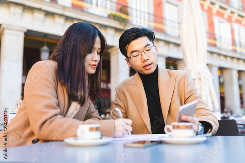 Spain, Madrid, young couple using cell phone and taking notes in a cafe at Plaza Mayor photo