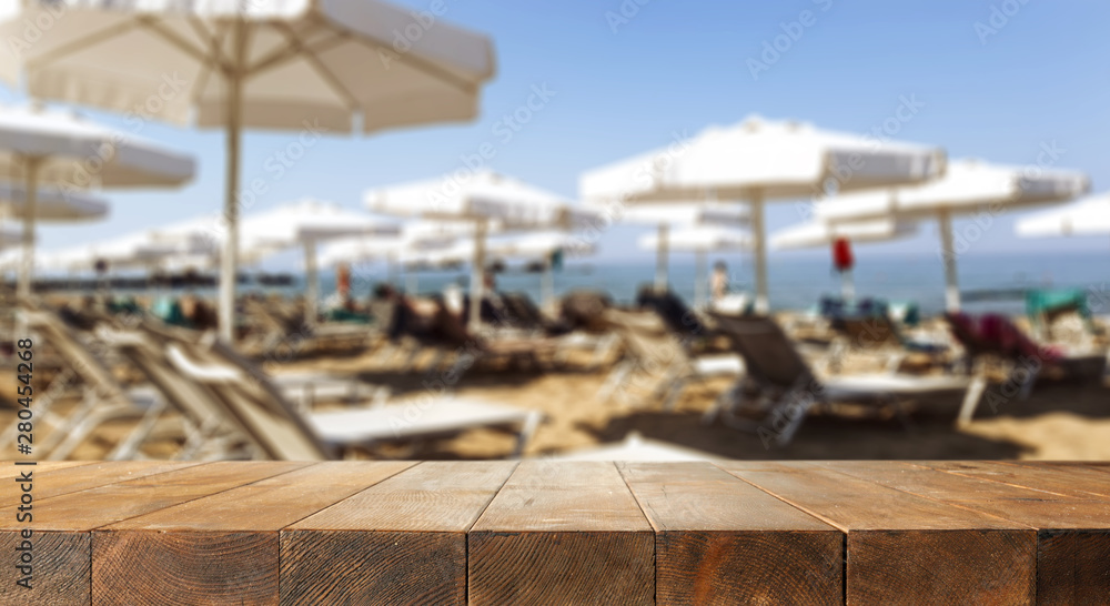 Table background with beautiful blue ocean and sandy beach view. Sun beds, umbrellas and the sea in distance. Summer sunny day.