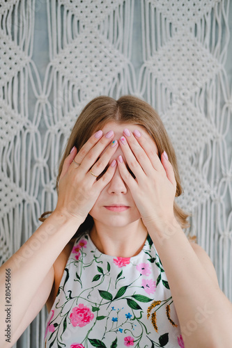 Portrait of a young woman covering her eyes with hands on background of macrame wall. photo