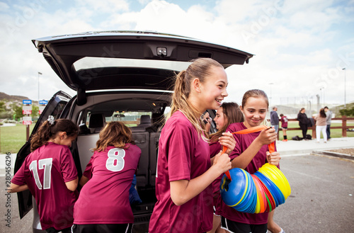 Fotografie Smiling girls carrying sports equipment with female unloading car in background