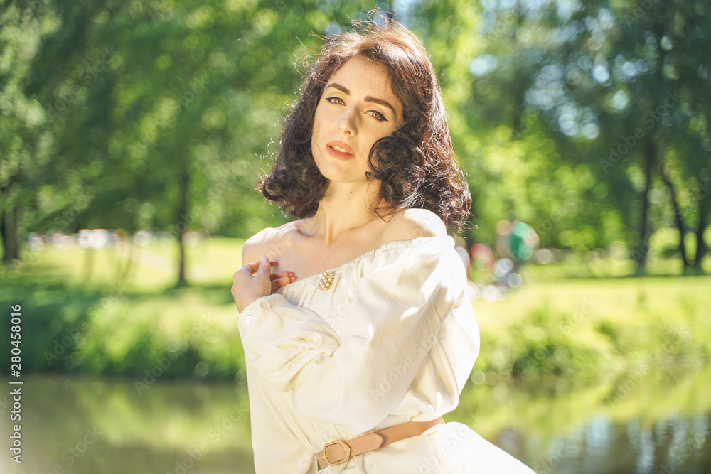 cute girl in a white summer dress tired of the sun and sat on a large stump near the lake in the shade of trees cute girl in a white summer dress tired of the sun and sat on a large stump near the lake in the shade of trees