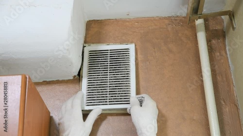  man in gloves opens a dusty ventilation grill to clean the ventilation 