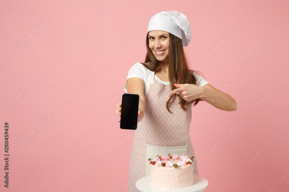 Chef cook confectioner or baker in apron white t-shirt, toque chefs hat cooking cake or cupcake at table hold cellphone isolated on pink pastel background in studio. Mock up copy space food concept. Chef cook confectioner or baker in apron white t-shirt, toque chefs hat cooking cake or cupcake at table hold cellphone isolated on pink pastel background in studio. Mock up copy space food concept.