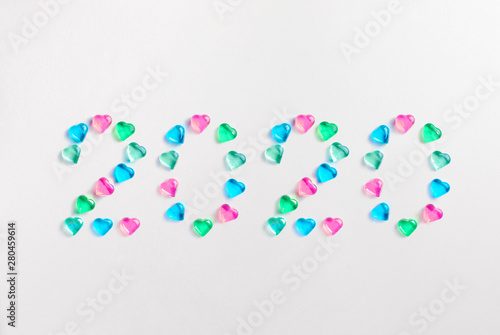 Happy New Year 2020. Symbol from number 2020 made of pastel colored decorative glass hearts laying on white paper background. Copy Space For Text. Minimal flat lay holiday concept.