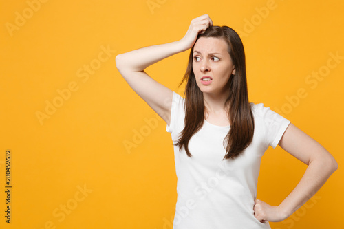 Portrait of preoccupied young woman in white casual clothes looking aside putting hand on head isolated on bright yellow orange wall background in studio. People lifestyle concept. Mock up copy space.