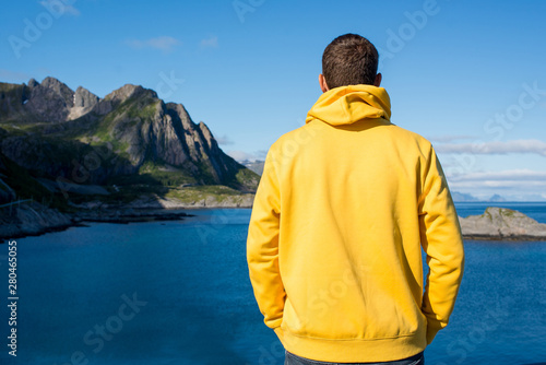 A young man in a yellow hoodie outdoor enjoy the northern beauty. Ocean and rocks landscape. Scenic view. Travel, adventure. Sense of freedom, lifestyle. Lofoten Islands, Norway. Summer in Scandinavia © Iuliia Pilipeichenko