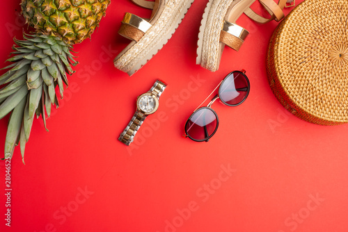 Wicker fashionable bag, sunglasses, tropical pineapple and expensive watches and women's shoes. Summer fashion, the concept of the holiday. On a bright red background. Banner