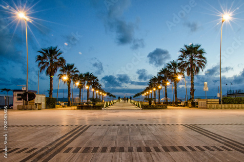  A warm evening on the Ligurian Sea in Italy. Palm trees at sunset. Flashing lights and palm trees. Sunset on the beach.