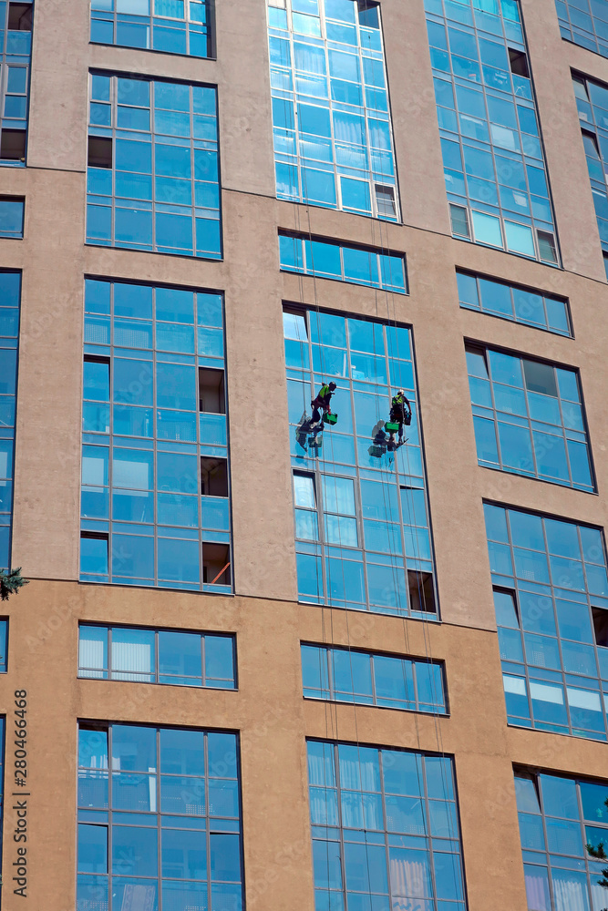 two industrial climbers wash windows in a high-rise building hanging from ropes two industrial climbers wash windows in a high-rise building hanging from ropes