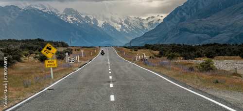 New Zealand road near Mount Cook (Aoraki) with motorcyclist and road sign “slippery when frosty” in New Zealand’s South Island