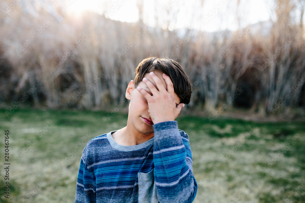 Boy outside appears sad as he covers part of his face with his hand Boy outside appears sad as he covers part of his face with his hand