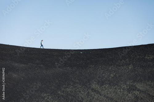 woman walks alone on a black basalt sand concave horizon line