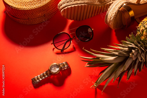 Flat lay, Wicker fashion bag, sunglasses, tropical pineapple and women's shoes. Summer fashion, holiday concept. On a bright red background. With hard light, Banner.