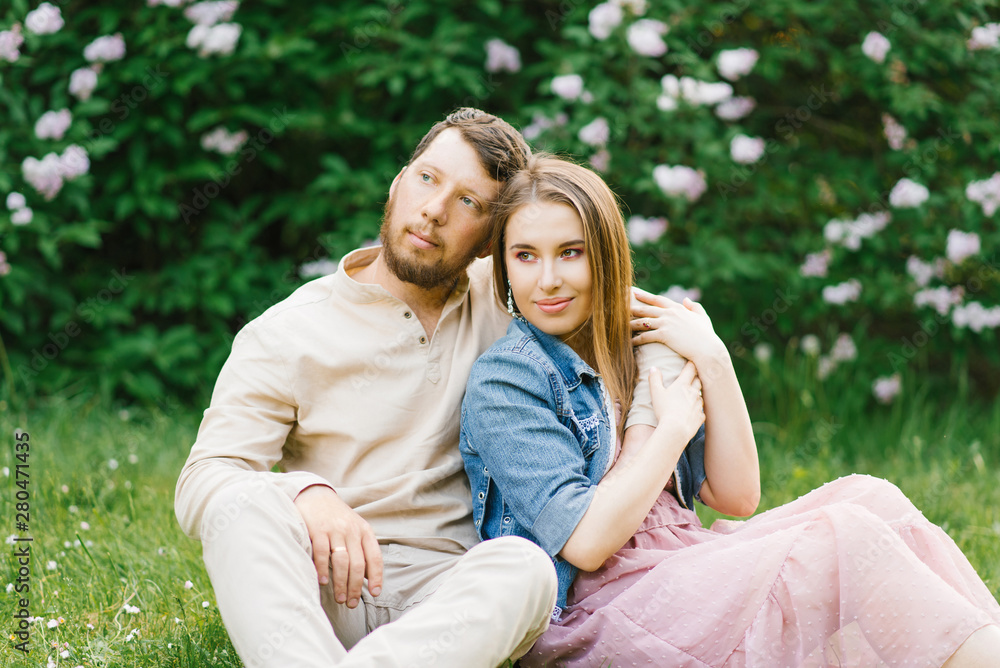 Lovers newlyweds on a romantic date sit on the grass in the spring, the guy hugs the girl, they enjoy and are happy to be together in love Lovers newlyweds on a romantic date sit on the grass in the spring, the guy hugs the girl, they enjoy and are happy to be together in love