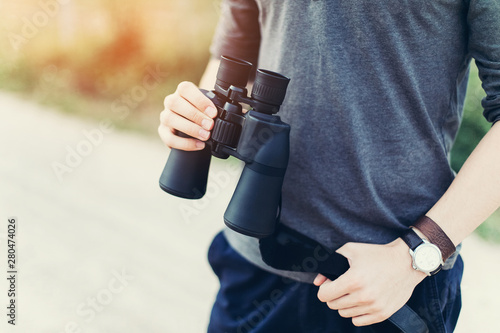 Young adventure man travelling holding binoculars in hands, watching landscape view outdoors. Young man discover nature scenes. Travelling, discovering, vacation concept