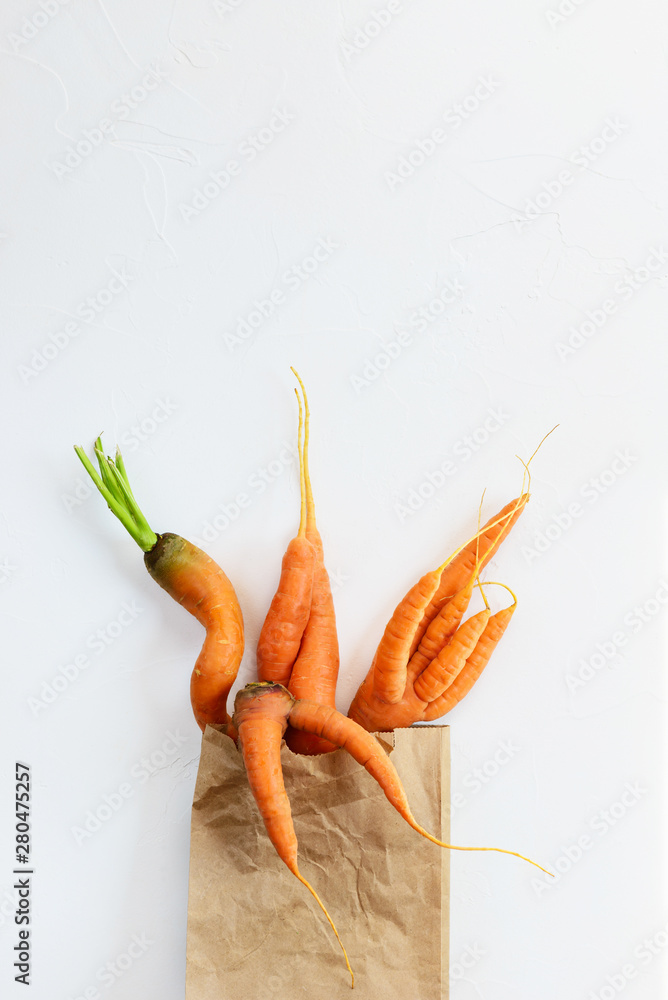 Ugly carrots in a paper bag. Ugly food, plastic free concept, flat lay