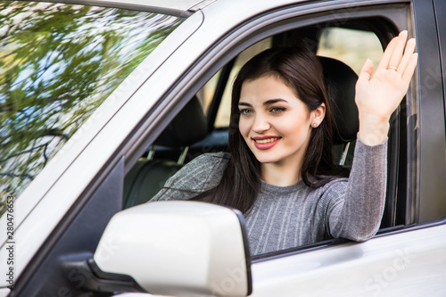 Hello. Beautiful young cheerful women looking at camera with smile and waving while sitting in her car