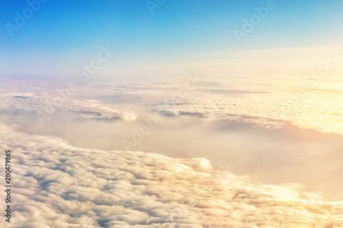 Beautiful scenic dramatic morning sunrise cloudscape aerial view from plane window. Gradient colored fluffy clouds during aircraft flight travel at sunset. Natural sky background