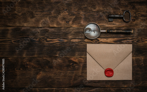 Photography Old envelope with a sealing wax stamp, rusty key and a magnifying glass on a brown wooden table background with a copy space