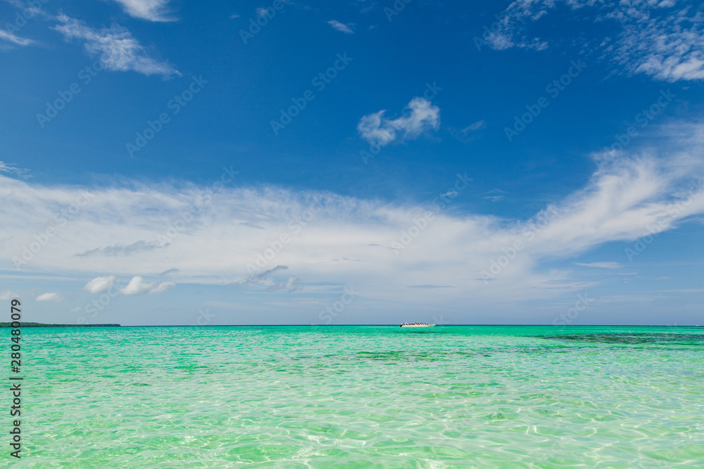 Empty white boat standing on the shore in the caribbean sea. Beautiful white sand beach, turquoise ocean and blue sky. Exotic background. Tropical travel concept and destination for vacation.