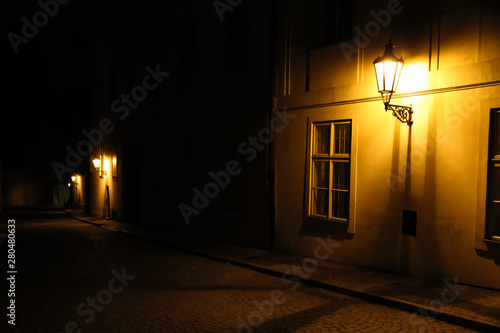 Old lanterns illuminating a dark alleyway medieval street at night in Prague, Czech Republic. Low key photo with brown yellow tones from the lanterns as single light sources against the dark shadows