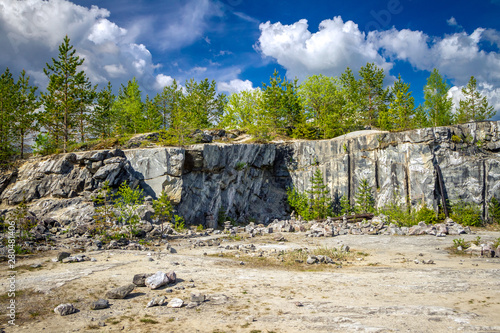 Marble rock with cracks. On the marble white and gray stains. The forest around. Ruskeala, Karelia.