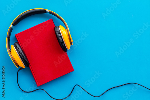 Books with headphones for listening to audiobook on blue background top view copy space photo