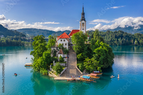 Bled, Slovenia - Aerial view of beautiful Pilgrimage Church of the Assumption of Maria on a small island at Lake Bled (Blejsko Jezero) and lots of Pletna boats on the lake at summer time with blue sky photo