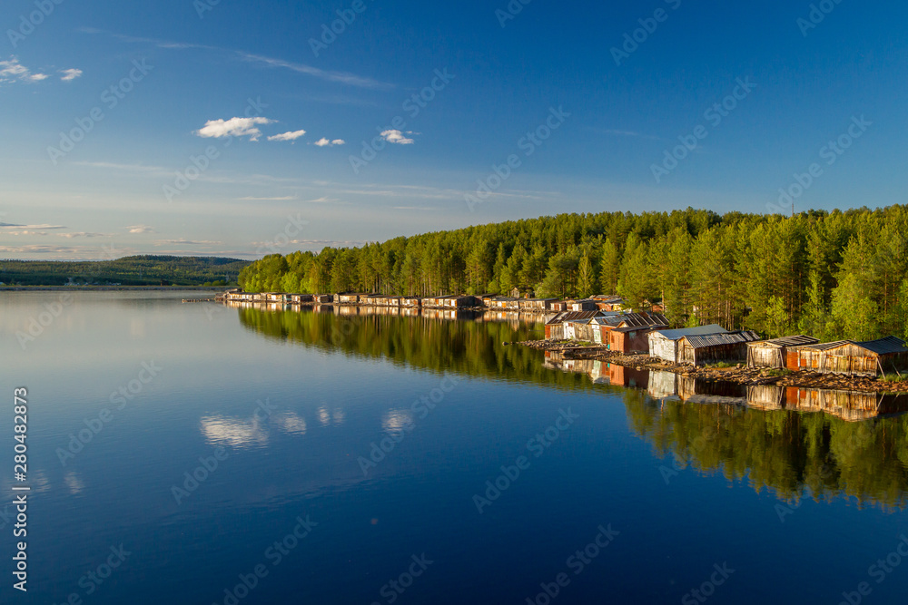 Old wooden boat sheds on Lake Kovdozero in the Murmansk region, Zelenoborsky village. The reflection in the water of trees and boat garages