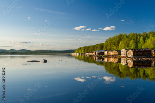 Old wooden boat sheds on Lake Kovdozero in the Murmansk region, Zelenoborsky village. The reflection in the water of trees and boat garages © Alexey Oblov