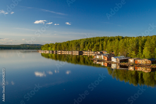 Old wooden boat sheds on Lake Kovdozero in the Murmansk region, Zelenoborsky village. The reflection in the water of trees and boat garages