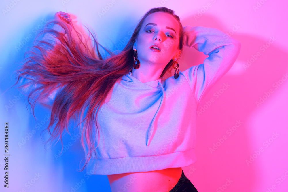 Fashion young elegant girl. Colored neon background, studio shot. Beautiful brunette woman. Hipster girl dancing in neon. Woman with stylish hair and red lips. Girl in a sweater and long hair.
