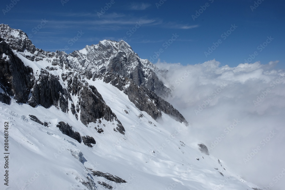 majestic white snow slope of Jade Dragon Snow Mountain in China Yunnan. Covered by wide white snow. sunny blue sky. Magnificent grey black rocks and boundless white cloud in sunshine