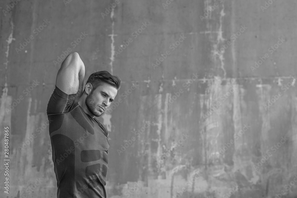 Black and white. Athlete doing stretching warmup exercise. Male fitness model in fashion sportswear in city. Runner sprinting on urban gray background. Black and white. Athlete doing stretching warmup exercise. Male fitness model in fashion sportswear in city. Runner sprinting on urban gray background.