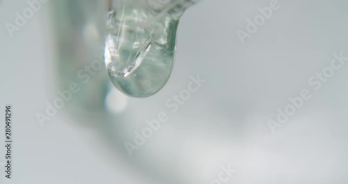 close up detail shot of two drops of transparent viscous liquid dripping down an edge. first drop is blurry in the background, the second drop is falling down slowly. art experimental footage photo