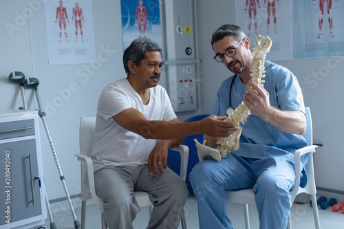 Male orthopedic surgeon explaining spine model to male patient photo