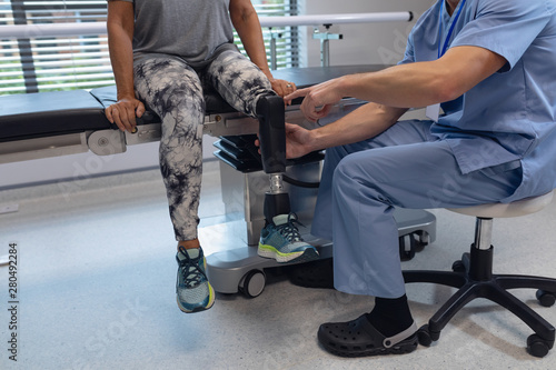 Male physiotherapist adjusting prosthetic leg of female patient in hospital photo