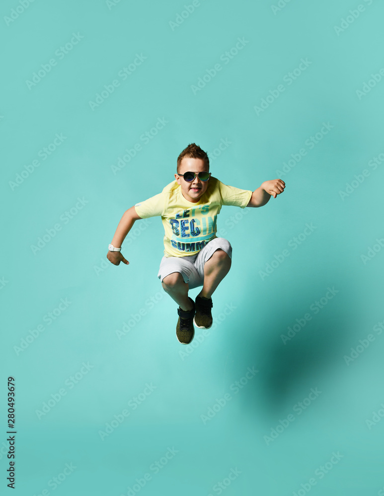 happy smiling boy jumping in the air in summer shorts and t-shirt, on turquoise background. happiness, childhood, freedom, movement and people concepts