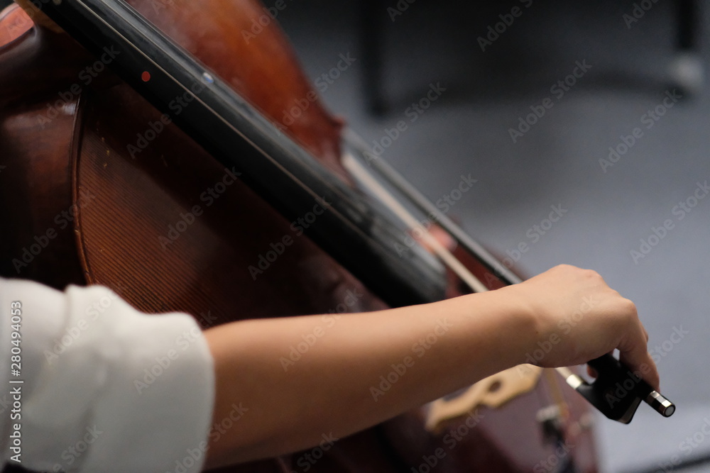 Close up female musician's arm taking a bow, playing brown cello. Blur background Close up female musician's arm taking a bow, playing brown cello. Blur background