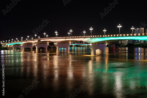 Long exposure of bridge in Nanning city Guangxi province China at night. Double cantilever reinforced concrete and Double column pier bridge. Brown and green reflection on river. Perspective