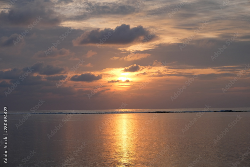 Burning rising sun above wide sea horizon. Gray cloud skyline. Bright yellow sunlight reflection on ocean surface.  Sunrise in Maldives