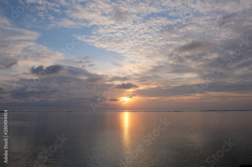 burning sun rising above sea horizon. white cloudy blue sky. bright yellow sunlight reflection on ocean surface. peaceful in Maldives. wide angle