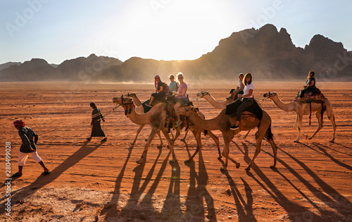 Women riding through the desert in Wadi Rum, Jordan, on camels lead by Bedouin guides.
