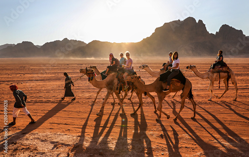 Women riding through the desert in Wadi Rum, Jordan, on camels lead by Bedouin guides.