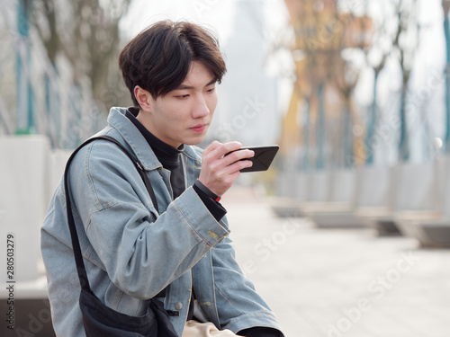 Portrait of a handsome Chinese young man holding his mobile phone, looking for something interesting in internet, mobile phone and the internet take up a lot of teenager's time.