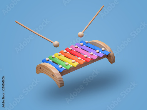Rainbow colored wooden toy xylophone hovers in the air with two sticks. Isolated on light blue background