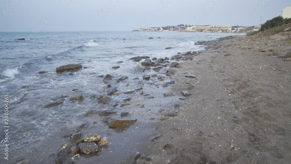 Light surf gently washes in as the cool morning light shines on the rocky beach looking toward Cala de Mijas on the Costa Del Sol in Southern Spain