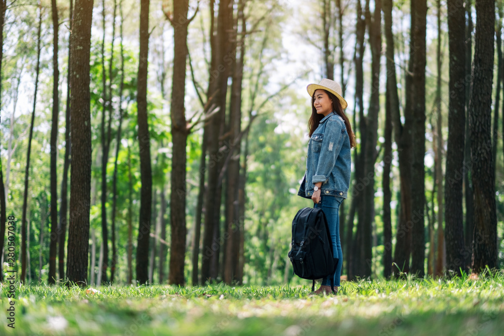 An asian female traveler with a hat and backpack looking into a beautiful pine woods