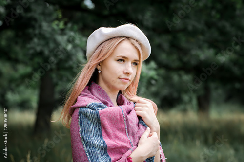 Young beautiful woman in a white beret holding a warm shawl in a cold forest